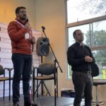 Rubén Carvacho dando su testimonio para Fundación Luz, de pie y con un hombre al lado también de pie