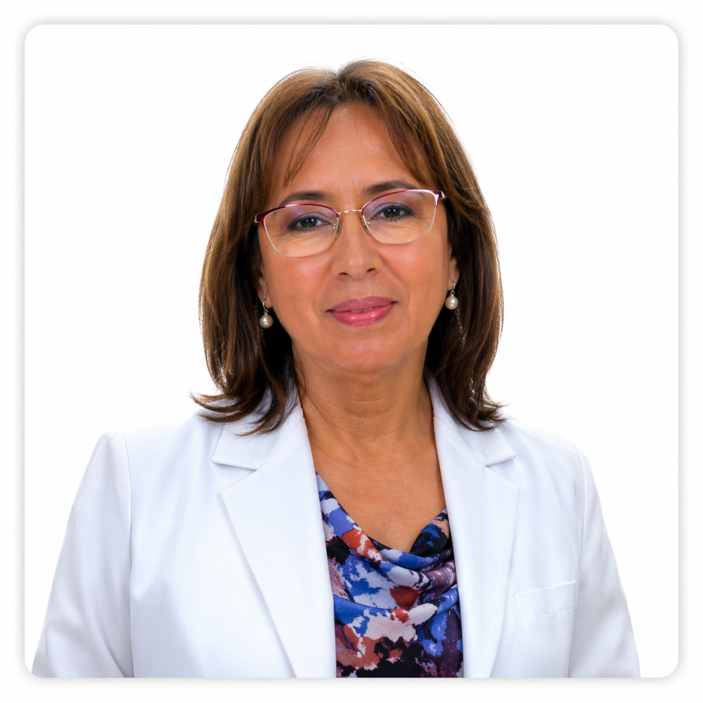 Mujer adulta con cabello castaño a la altura de los hombros, usa lentes y aros pequeños. Viste blazer blanco sobre una blusa con estampado azul y rosado, y mira a la cámara con una expresión amable.