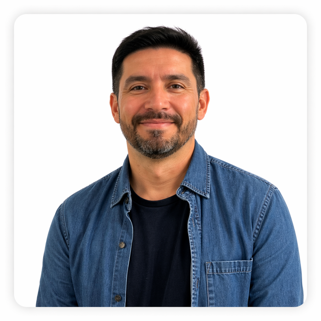 Hombre adulto con cabello corto oscuro y barba recortada. Viste una camisa de mezclilla azul sobre una polera oscura y sonríe levemente mirando al frente.